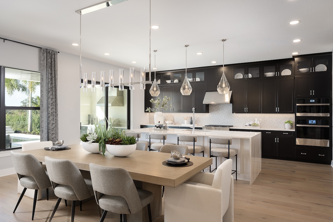 Luxury kitchen design featuring black cabinets, waterfall island and wooden dining table. 