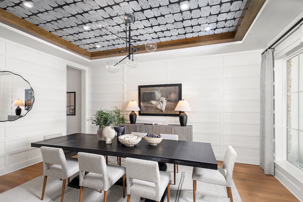 Bright and contemporary dining space with white grid-paneled walls, statement ceiling design in gray and wood tones, and a sleek black dining table surrounded by neutral chairs.